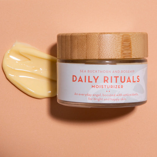 Jar of Daily Rituals moisturizer by The Organic Skin Co. with a wooden lid on a peach background