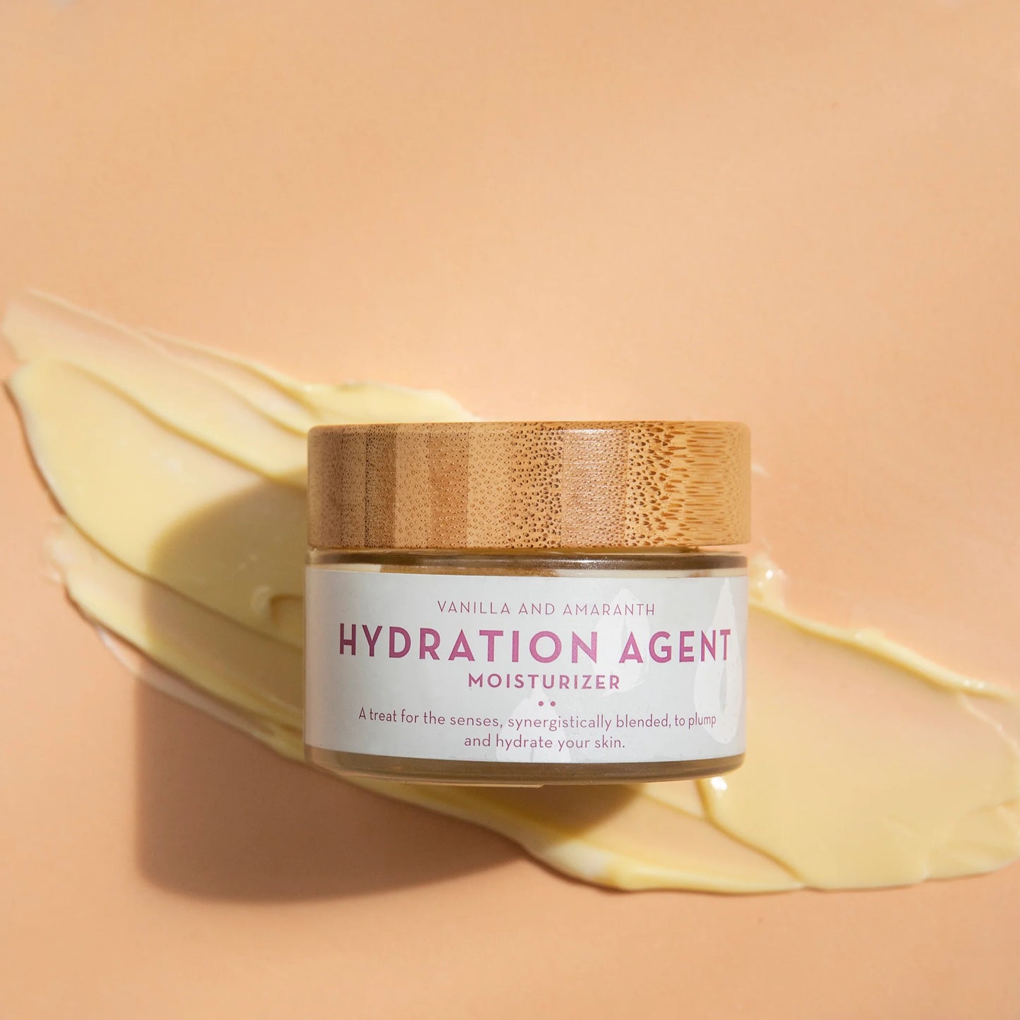 Jar of Hydration Agent moisturizer by The Organic Skin Co. with a wooden lid on a peach background