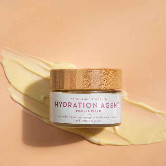 Jar of Hydration Agent moisturizer by The Organic Skin Co. with a wooden lid on a peach background