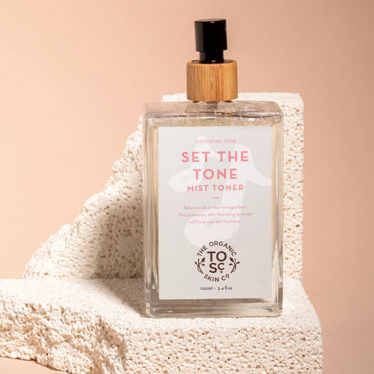 Mist toner bottle labeled Set the Tone by The Organic Skin Co. on a textured surface with a beige background.