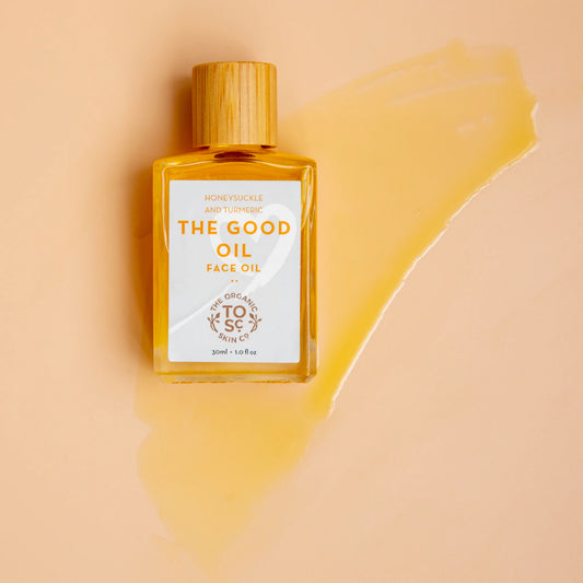 Bottle of The Good Oil face oil by The Organic Skin Co. with a wooden cap on a beige background